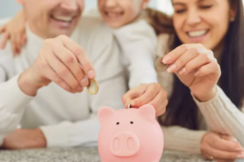 Pais e filha sorridentes a colocar moedas num mealheiro cor-de-rosa
